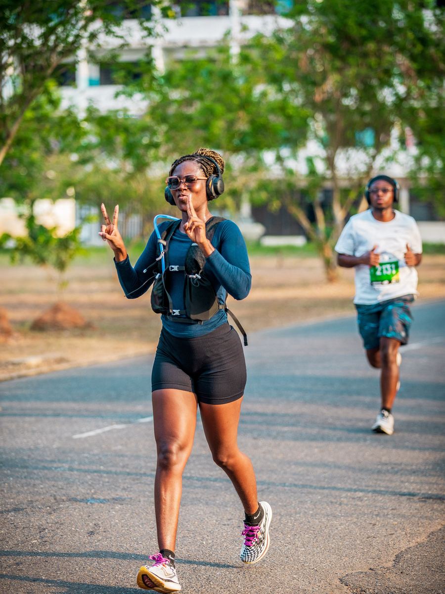 A runner throwing a peace sign on a tree-lined road mid-race